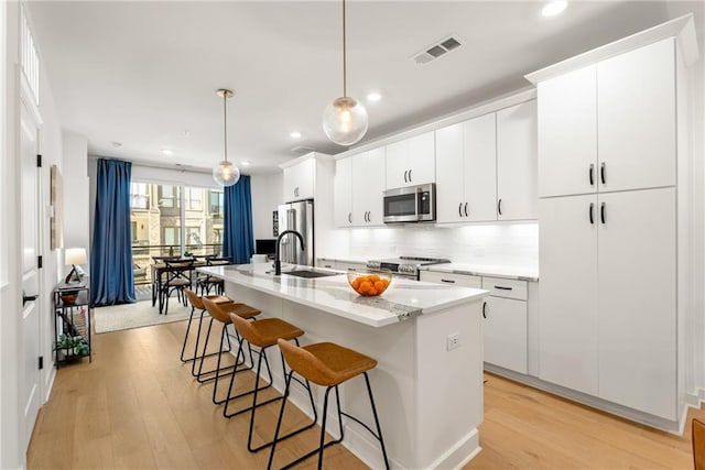 kitchen with a center island with sink, hanging light fixtures, appliances with stainless steel finishes, light hardwood / wood-style floors, and white cabinetry