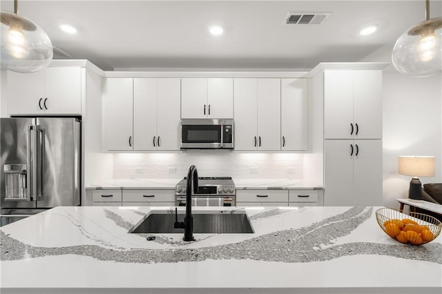 kitchen featuring decorative backsplash, light stone countertops, decorative light fixtures, white cabinetry, and stainless steel appliances