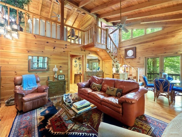 living room featuring ceiling fan, beamed ceiling, light hardwood / wood-style flooring, wood walls, and wooden ceiling