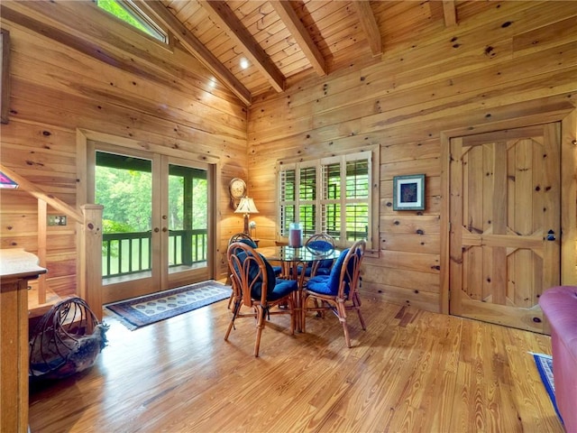 dining room with wooden walls, beam ceiling, high vaulted ceiling, wooden ceiling, and light hardwood / wood-style flooring