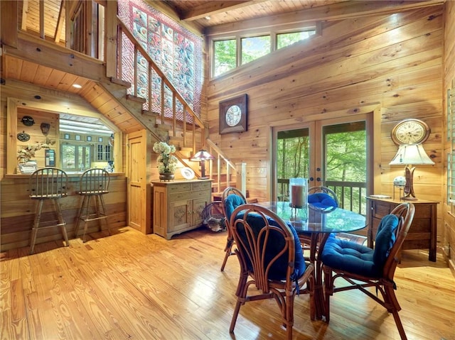 dining area featuring a high ceiling, wood walls, light hardwood / wood-style flooring, and french doors