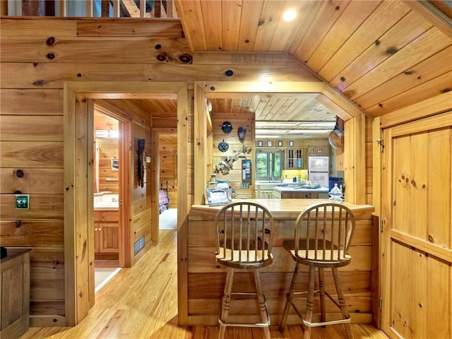 bar featuring wood walls, vaulted ceiling, wooden ceiling, and light wood-type flooring