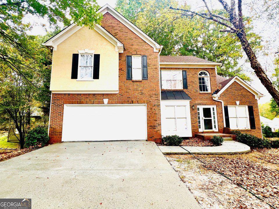 view of front facade featuring driveway, stucco siding, an attached garage, and brick siding