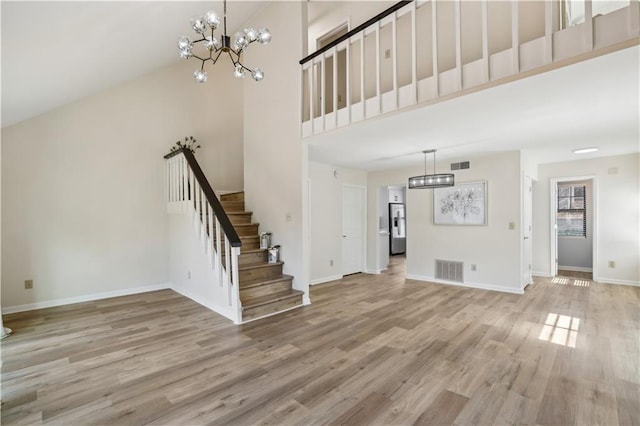 unfurnished living room with visible vents, stairway, a high ceiling, and wood finished floors