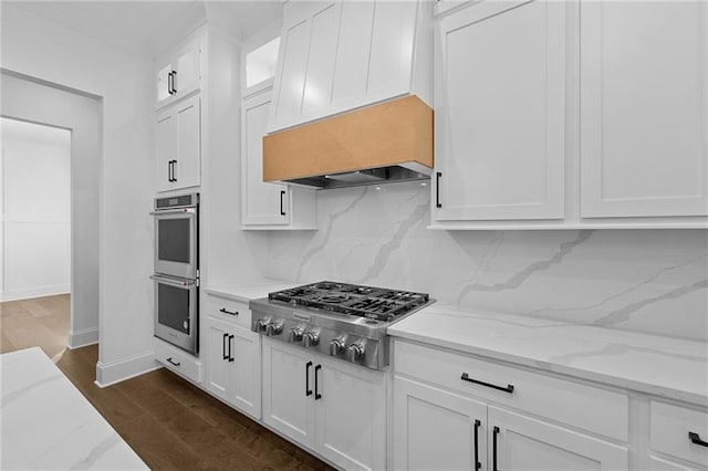 kitchen featuring light stone counters, premium range hood, stainless steel appliances, white cabinetry, and tasteful backsplash