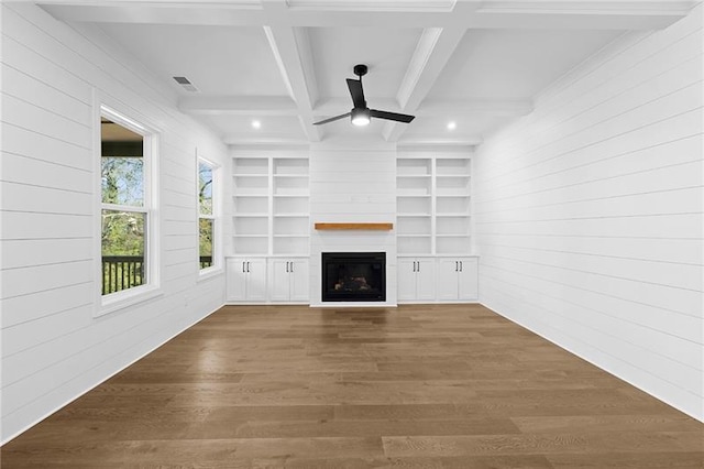 unfurnished living room featuring wooden walls, a large fireplace, a ceiling fan, wood finished floors, and beamed ceiling