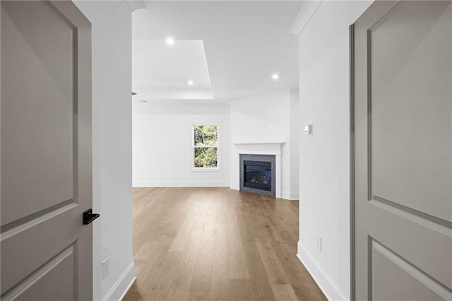 unfurnished living room featuring wood finished floors, baseboards, a glass covered fireplace, a tray ceiling, and recessed lighting