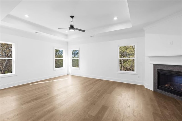unfurnished living room featuring a tray ceiling, a wealth of natural light, ceiling fan, and hardwood / wood-style floors