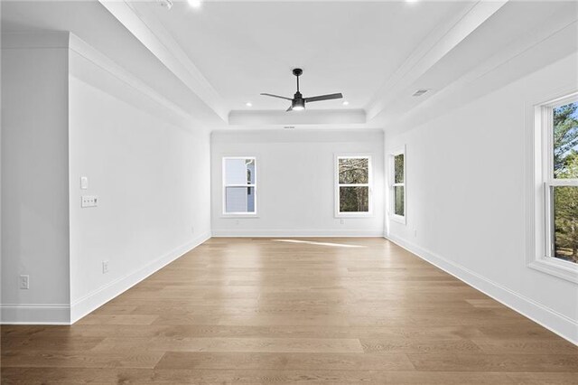 empty room with light wood-style floors, ceiling fan, and a tray ceiling