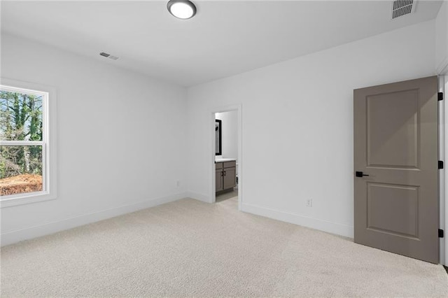 unfurnished bedroom featuring visible vents, baseboards, ensuite bathroom, and light colored carpet
