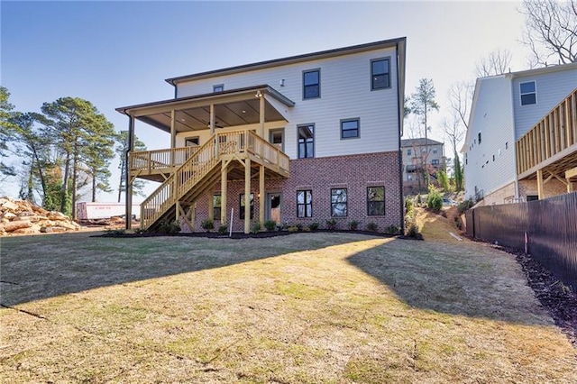 back of property featuring fence, a deck, brick siding, a lawn, and stairway