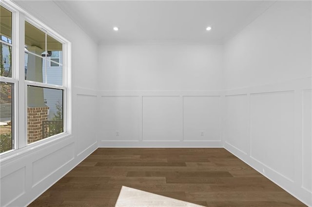 empty room featuring crown molding, dark wood-style flooring, a wainscoted wall, and a decorative wall