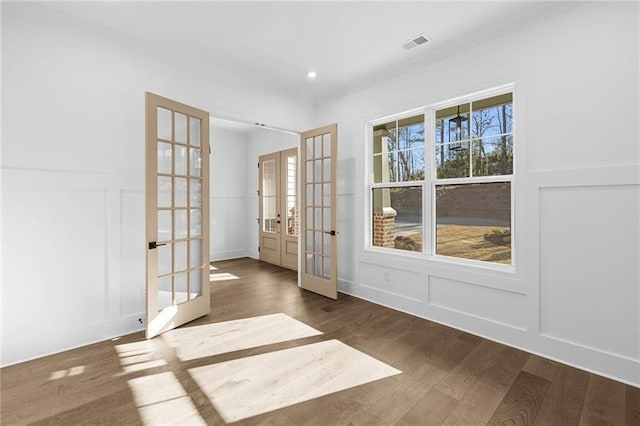 unfurnished room with visible vents, ornamental molding, a decorative wall, wood finished floors, and french doors