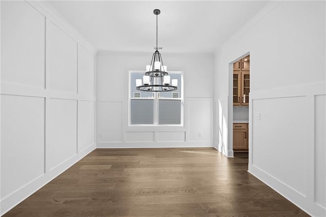 unfurnished dining area featuring an inviting chandelier, a decorative wall, and dark wood-style floors