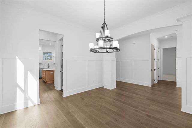 unfurnished dining area featuring dark wood-type flooring, a decorative wall, a wainscoted wall, and a notable chandelier