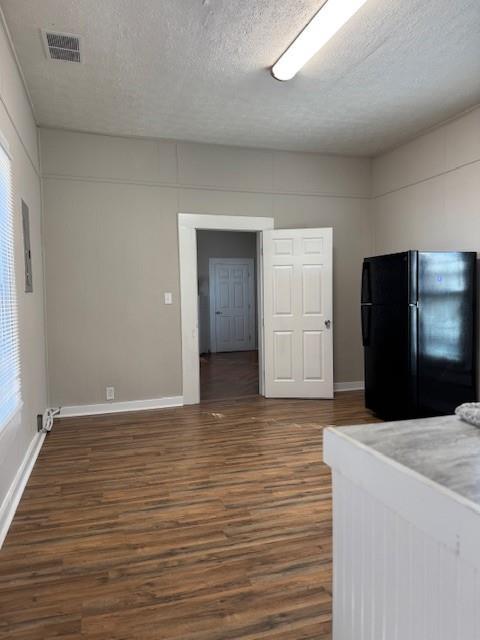 unfurnished bedroom featuring a textured ceiling, black fridge, and dark wood-type flooring