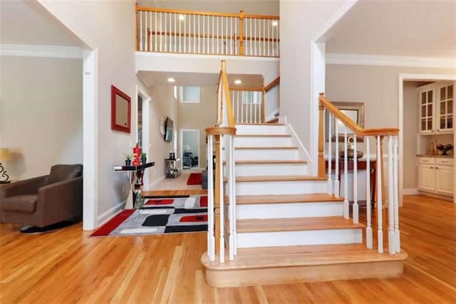 stairs featuring hardwood / wood-style floors, a towering ceiling, and ornamental molding