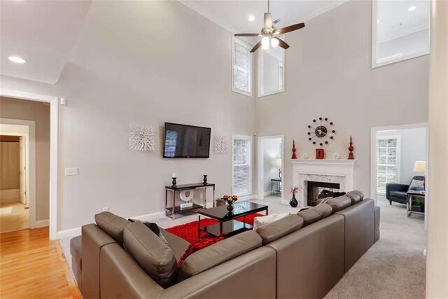 living room featuring a high end fireplace, ceiling fan, light wood-type flooring, and a high ceiling