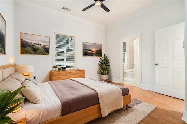 bedroom with ornamental molding, connected bathroom, light wood-style floors, visible vents, and ceiling fan
