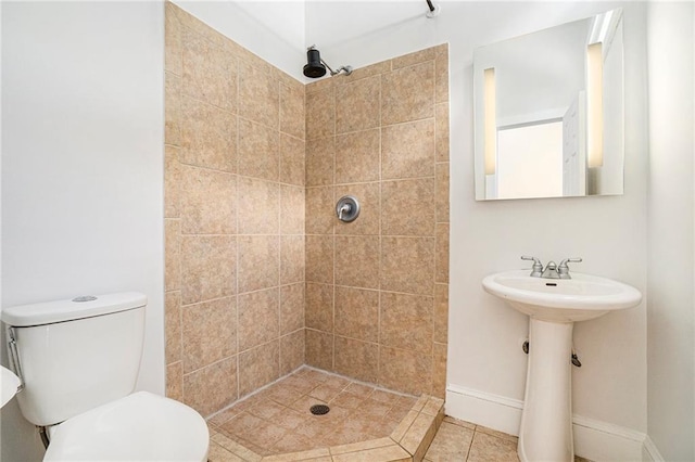 bathroom featuring baseboards, tile patterned flooring, toilet, tiled shower, and a sink
