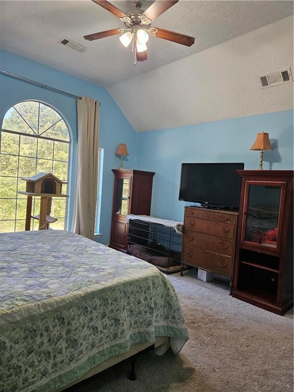 bedroom with a textured ceiling, vaulted ceiling, ceiling fan, and carpet floors