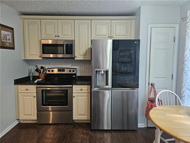 kitchen with stainless steel appliances, a textured ceiling, dark hardwood / wood-style flooring, dark stone countertops, and cream cabinetry