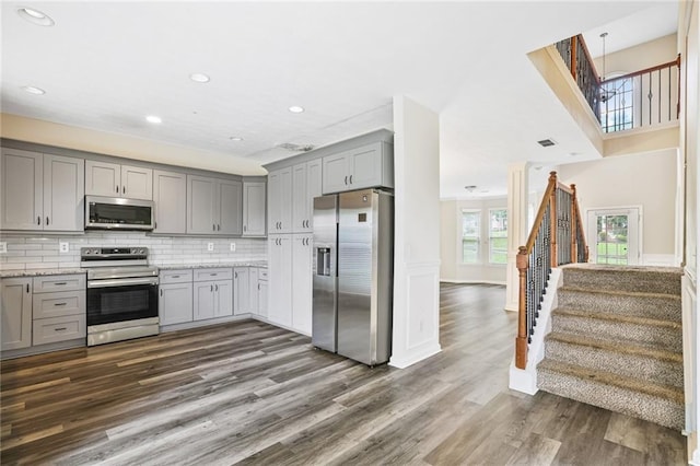 1212 Ashton Park Dr, Lawrenceville, GA 30045 - kitchen with stainless steel appliances, gray cabinets, dark wood-style flooring, decorative backsplash, and light stone countertops