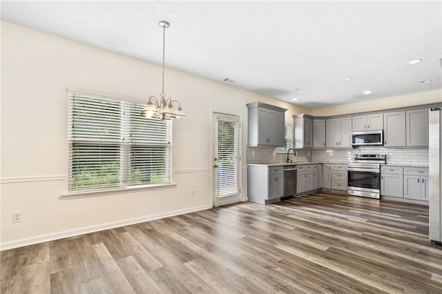 1212 Ashton Park Dr, Lawrenceville, GA 30045 - kitchen with appliances with stainless steel finishes, gray cabinets, a chandelier, backsplash, and wood finished floors