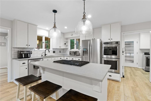 kitchen with tasteful backsplash, decorative light fixtures, light wood-type flooring, appliances with stainless steel finishes, and white cabinets