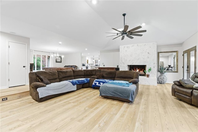 living room featuring lofted ceiling, ceiling fan with notable chandelier, a fireplace, and light hardwood / wood-style floors