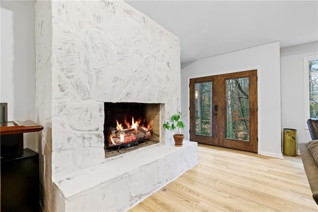 living room with a stone fireplace, light hardwood / wood-style flooring, and french doors