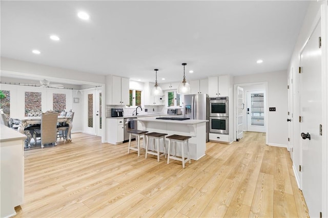 kitchen with light hardwood / wood-style flooring, stainless steel appliances, a center island, tasteful backsplash, and white cabinets