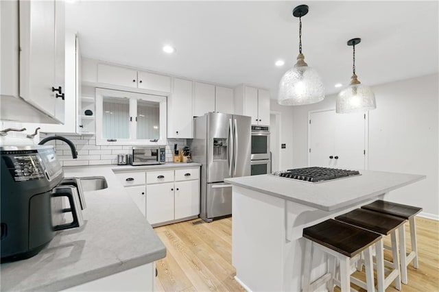 kitchen with a kitchen island, appliances with stainless steel finishes, pendant lighting, white cabinetry, and sink