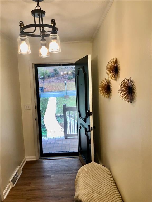 doorway to outside with crown molding, dark wood-type flooring, and an inviting chandelier