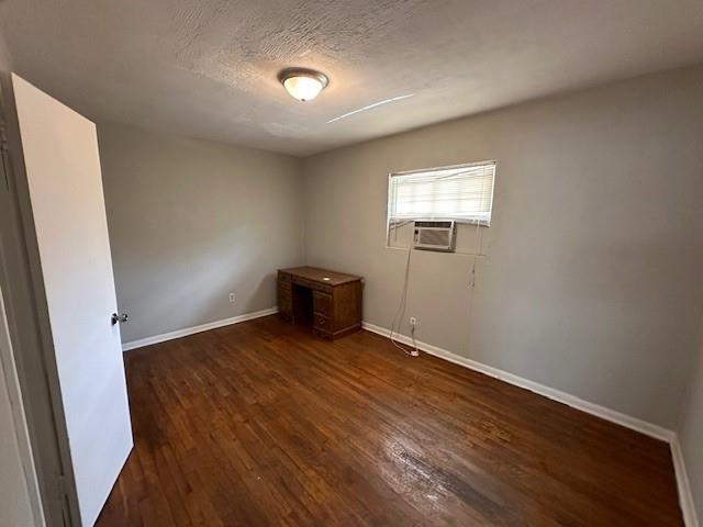 unfurnished room with dark wood-type flooring, cooling unit, baseboards, and a textured ceiling