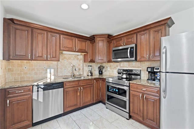 kitchen with sink, light tile patterned floors, appliances with stainless steel finishes, light stone countertops, and decorative backsplash