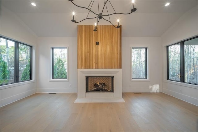 unfurnished living room with a wealth of natural light, wood finished floors, vaulted ceiling, and baseboards
