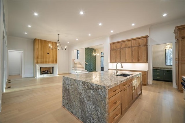 kitchen featuring ornamental molding, a chandelier, a fireplace, an island with sink, and a sink