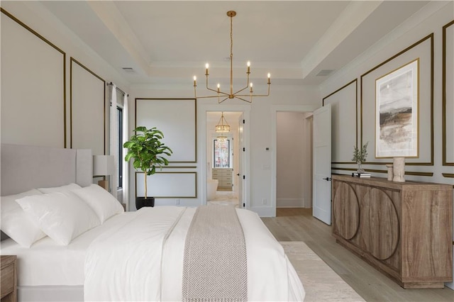 bedroom featuring crown molding, a decorative wall, light wood-style flooring, a tray ceiling, and a notable chandelier