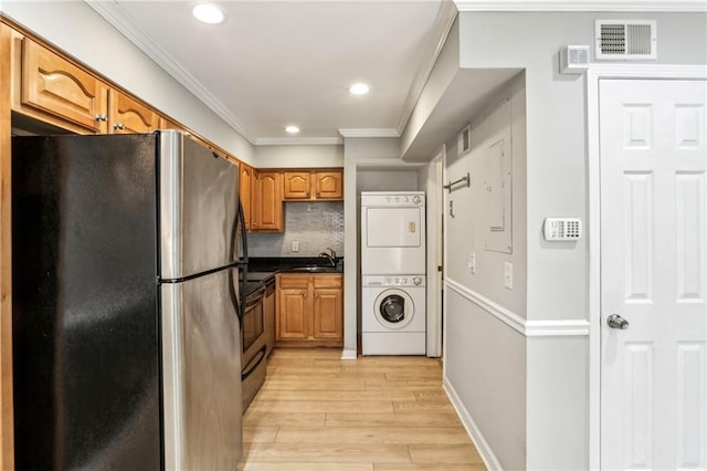 kitchen featuring appliances with stainless steel finishes, decorative backsplash, stacked washer / drying machine, crown molding, and light wood-type flooring