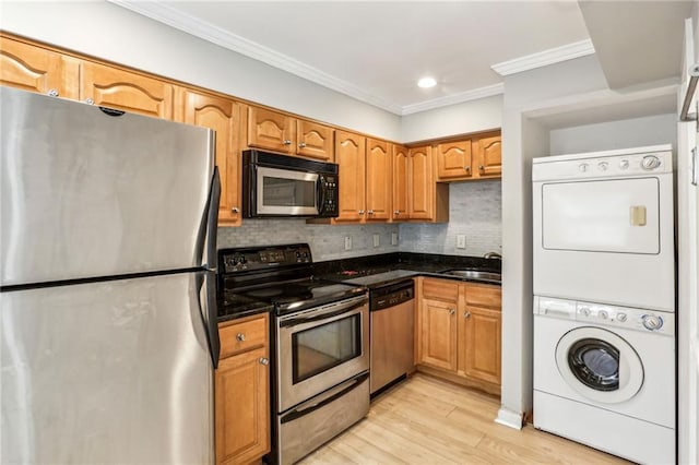 kitchen with stacked washer and dryer, appliances with stainless steel finishes, sink, and dark stone counters