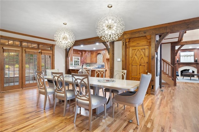 dining area featuring a chandelier, light wood finished floors, ornamental molding, french doors, and a fireplace