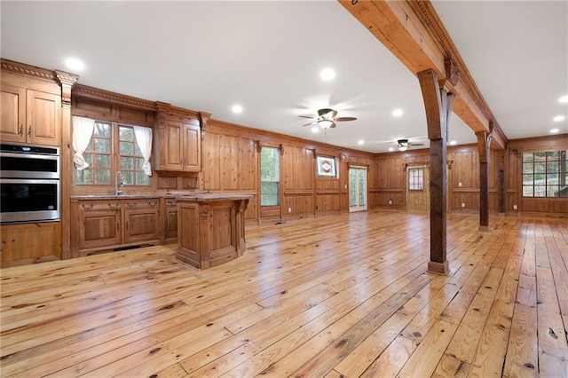 kitchen with open floor plan, light wood finished floors, double oven, a ceiling fan, and ornamental molding