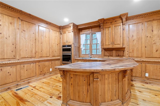 kitchen with a sink, light wood-type flooring, stainless steel double oven, wood counters, and wooden walls