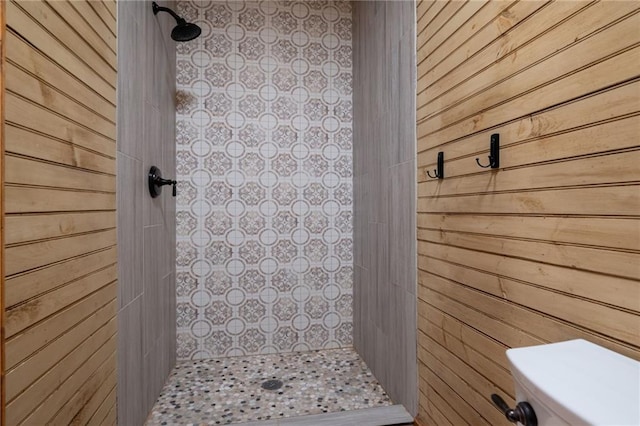 bathroom featuring tiled shower, wooden walls, and toilet