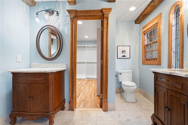 bathroom featuring two vanities, baseboards, recessed lighting, and toilet