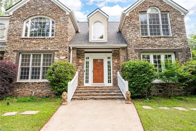 view of front of home with a front yard, stone siding, and a shingled roof