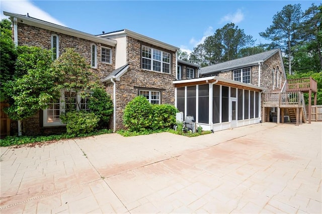 rear view of house with a sunroom, stone siding, and stairs