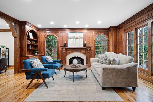 living room with crown molding, light wood-style floors, a fireplace, wood walls, and recessed lighting