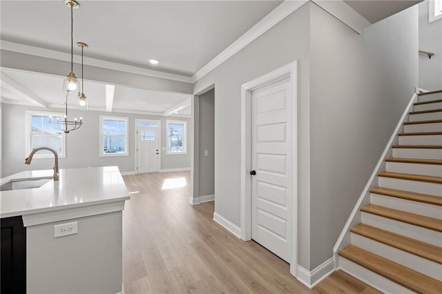 kitchen featuring pendant lighting, sink, light hardwood / wood-style flooring, beam ceiling, and ornamental molding